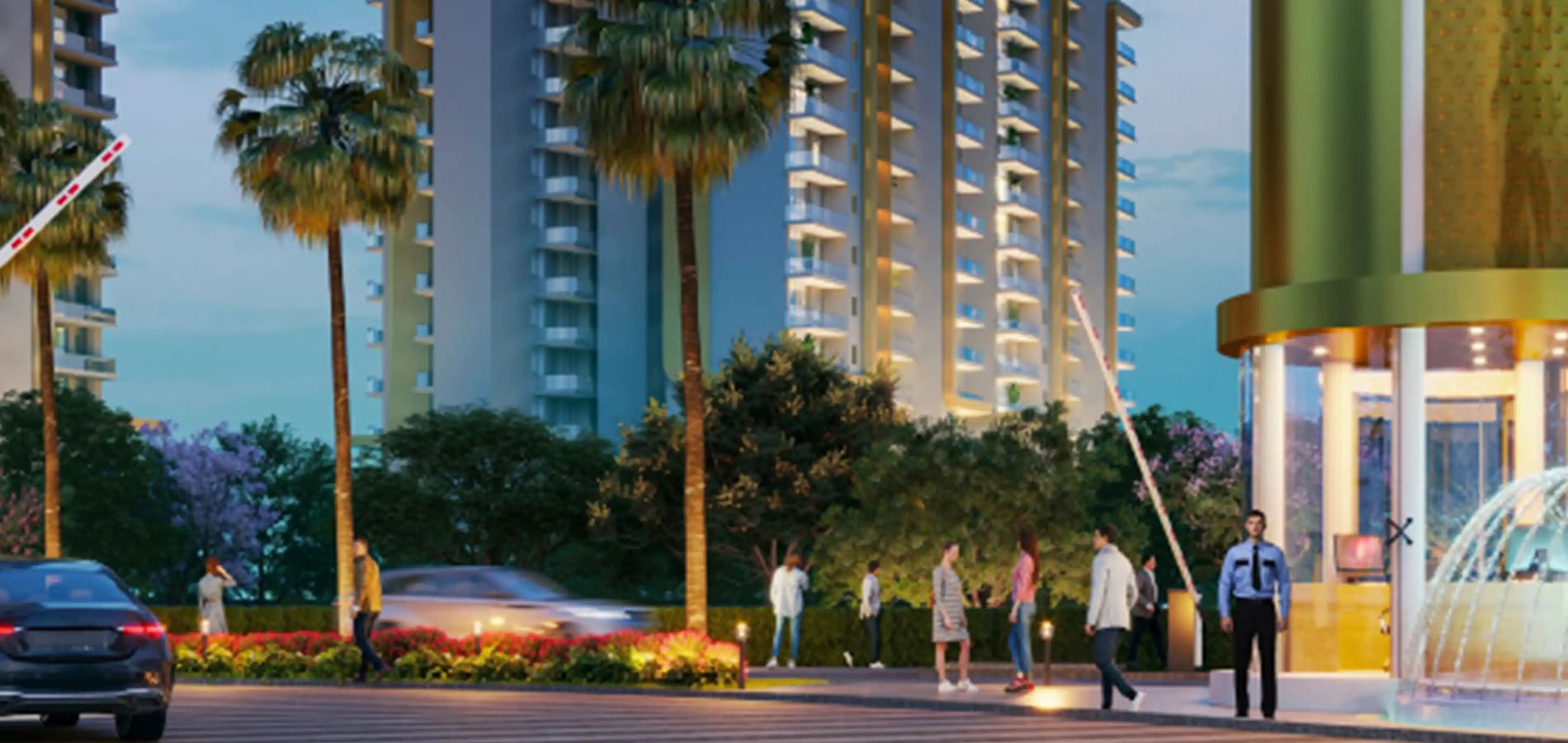 Main entrance walkway of the residential complex featuring a water fountain structure, palm trees, and residents walking at dusk