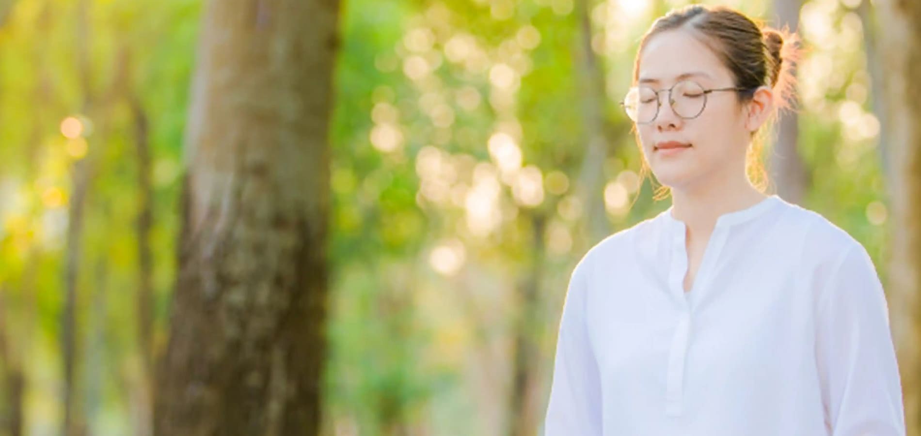 Serene close-up of a woman meditating with closed eyes in a tranquil, sunlit forest setting